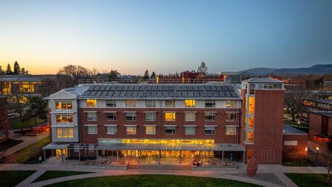 A UO residence hall at dusk with lights on in the windows.