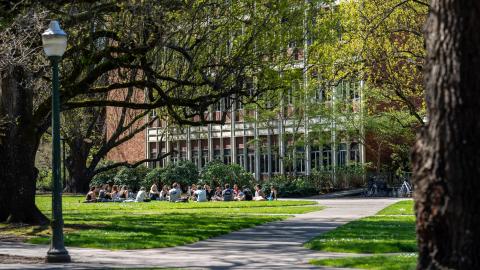 Students sit in a circle outside a campus building on a sunny day.