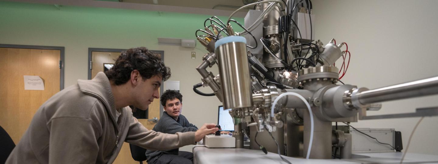 Two students sit at a workstation, adjusting an instrument in the Center for Advanced Materials Characterization in Oregon.
