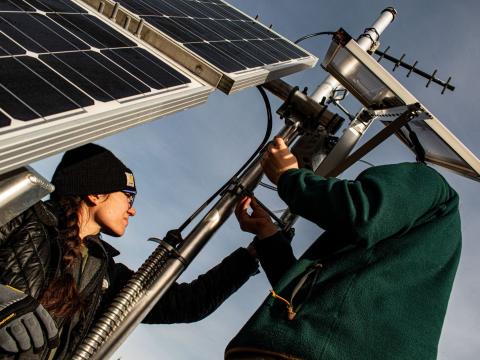 Two people installing a solar powered camera on a tower.