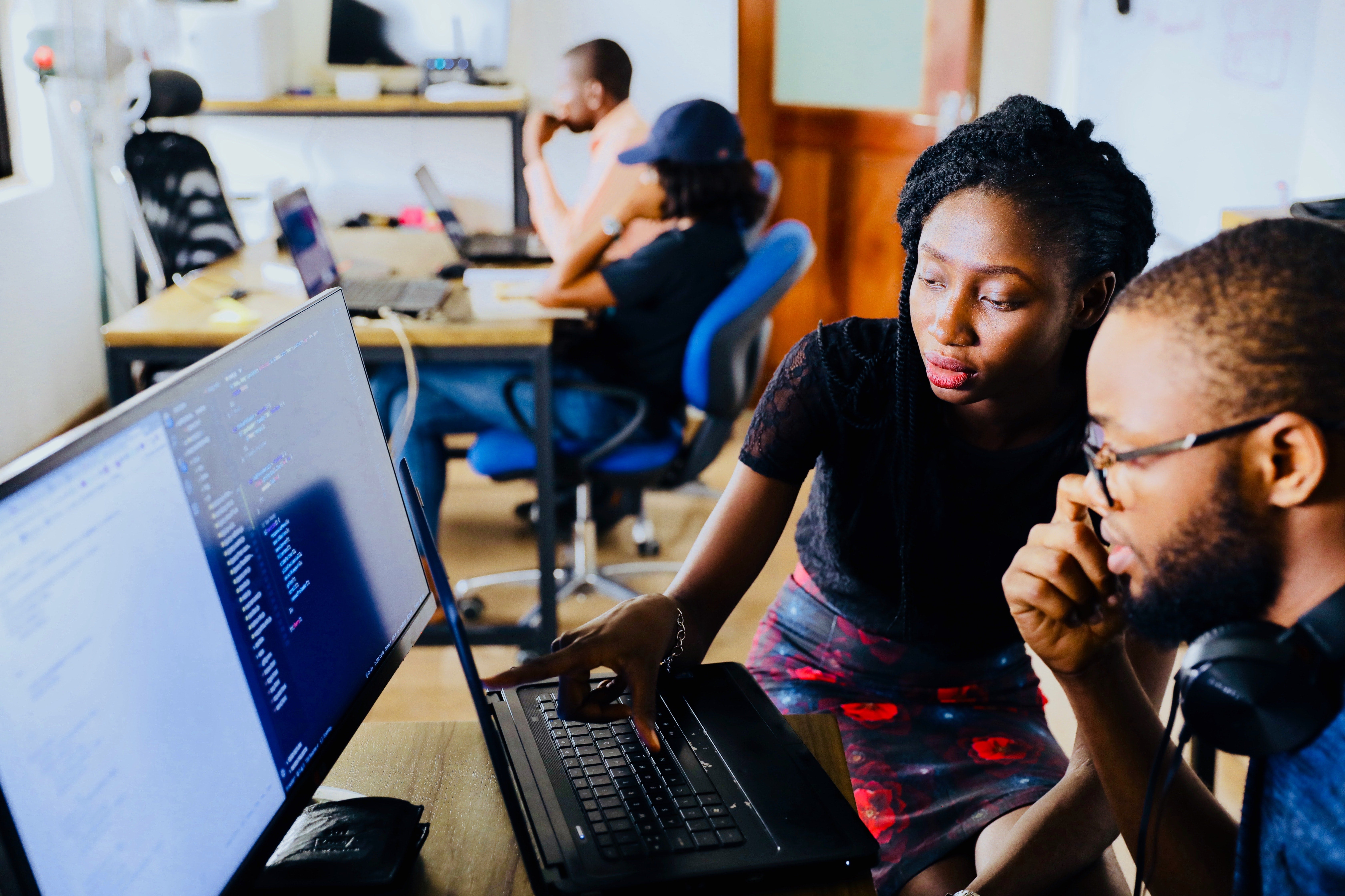 A Black woman and a Black man working together on a computer that is displaying code