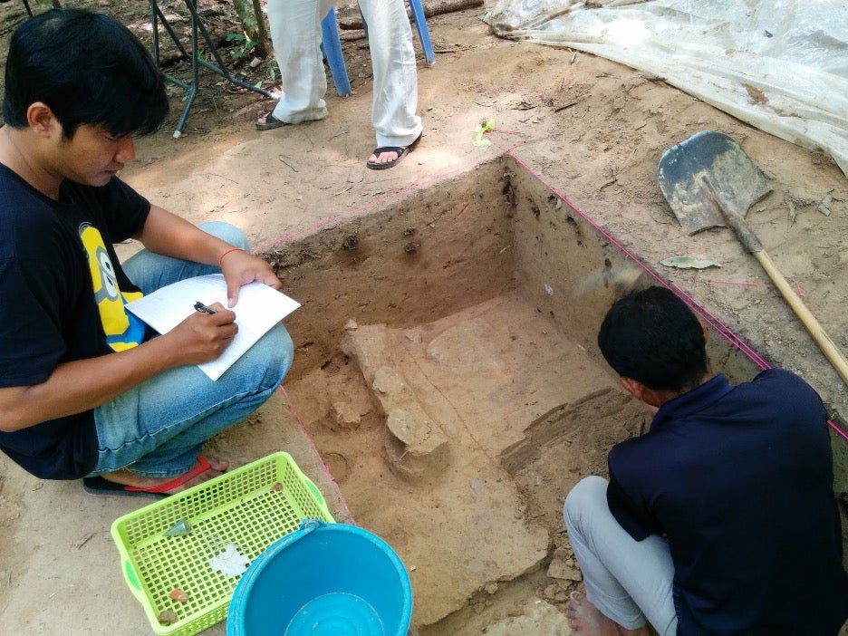 Archaeologists excavate a site. One person takes detailed notes in a notebook while the other digs.