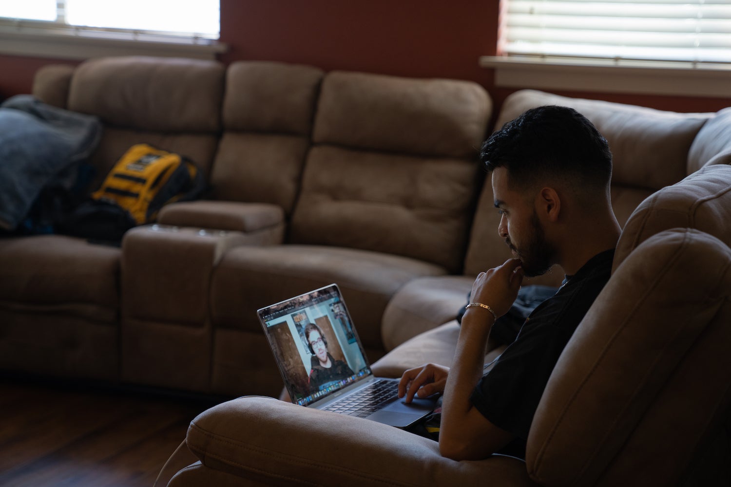 A person sitting on a couch looks at a computer screen, on which there is a Zoom call occurring.