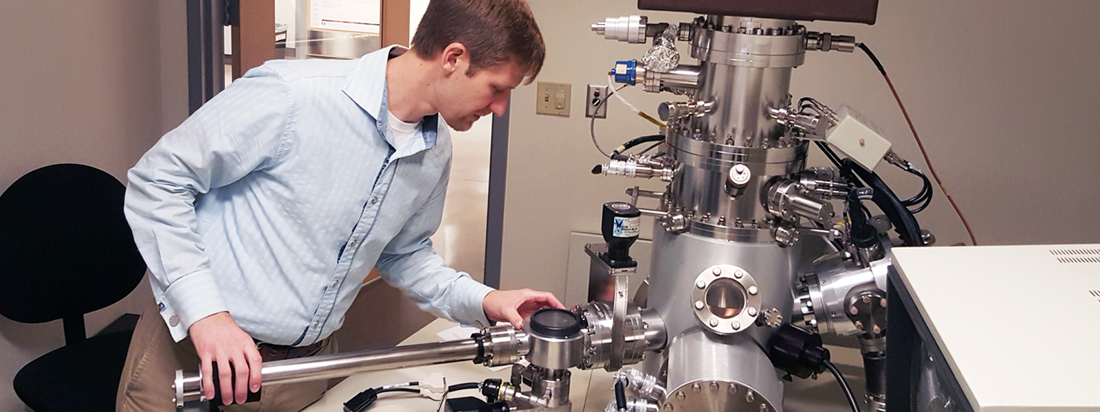 A man makes small adjustments to a machine in the Center for Advanced Materials Characterization in Oregon.