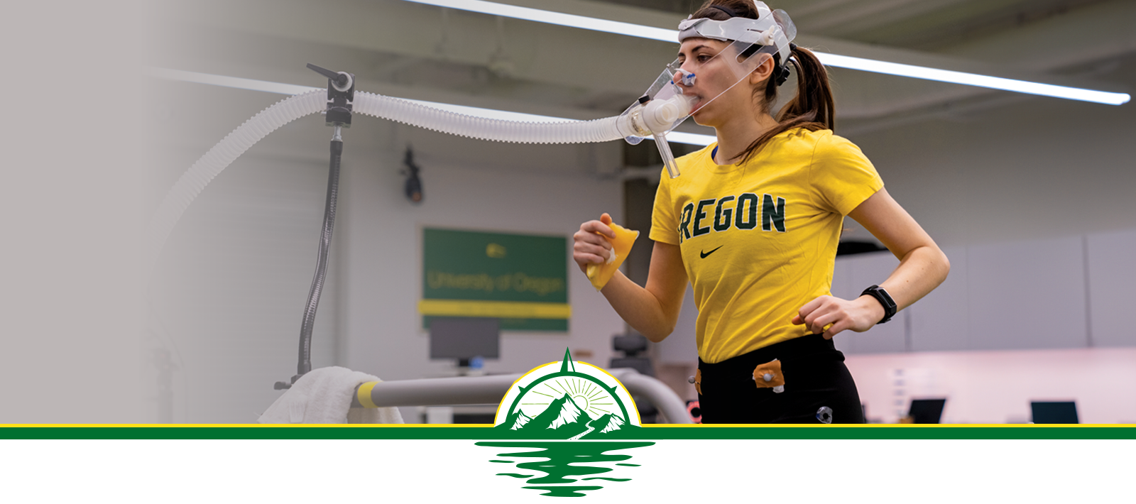 Woman wearing a yellow Oregon T-shirt running on a treadmill with devices attached to her face and body for research.