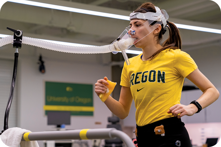 Woman runs on a treadmill while wearing a mask to measure respiratory gas exchange.