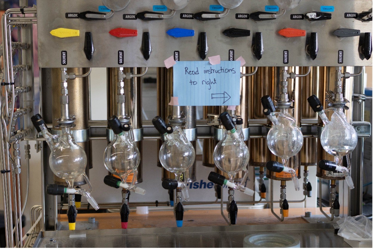 A machine with different colored levers and glass bottles. A sign is taped on it that says ‘read instructions to right’ with an arrow.