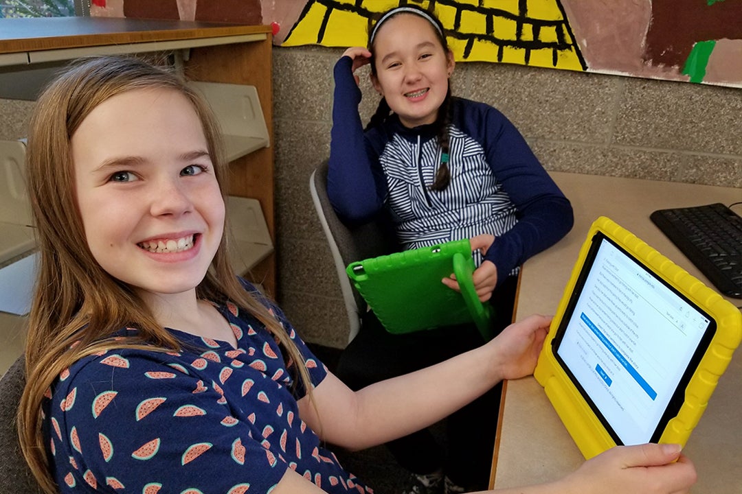 Two girls smiling with tablets in their hands.