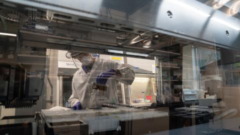 A person in a white lab coat and personal protective equipment in a laboratory works with samples in the Monitoring and Assessment Program, part of the UO's COVID-response.