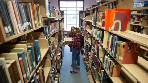 Two women stand between shelves of books in the library.