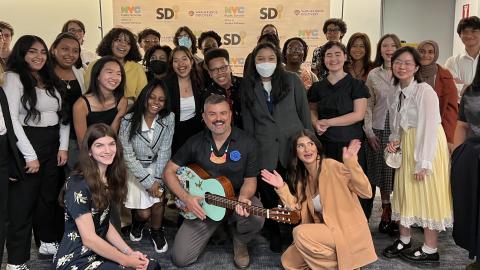 A large group of students surrounding Ernesto Martínez who is holding a painted guitar. 