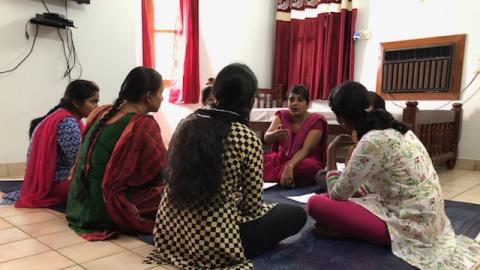 Women gather in a seated circle around a woman who is talking.