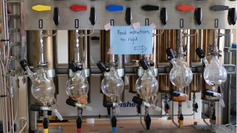 A machine with different colored levers and glass bottles. A sign is taped on it that says ‘read instructions to right’ with an arrow.