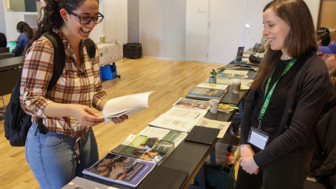 Two women talking on opposite sides of a table at an informational event
