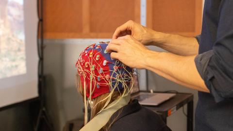Research participant sits in a chair and has an electroencephalogram (EEG) cap placed on their head.  