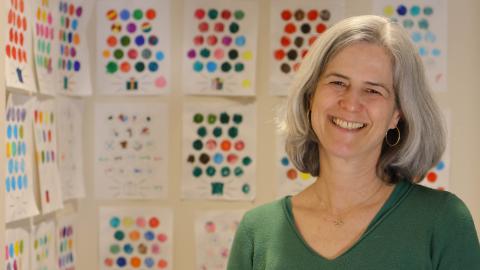 Melissa Redford posing next to a wall of colorful worksheets that children use to keep track of their progress in the study.