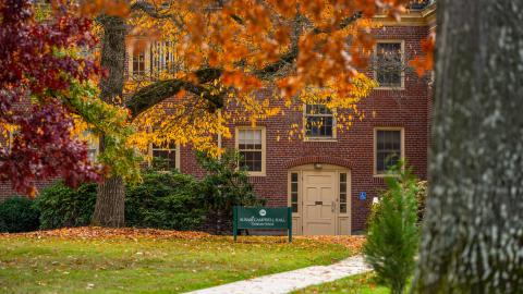Trees full of bright red and orange fall leaves frame a red brick building.