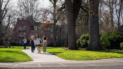 Students walking on a campus path between buildings on a sunny winter day.