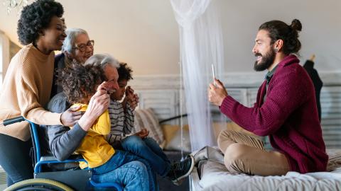 A person sitting on a bed takes a photo of a group of smiling kids and adults.