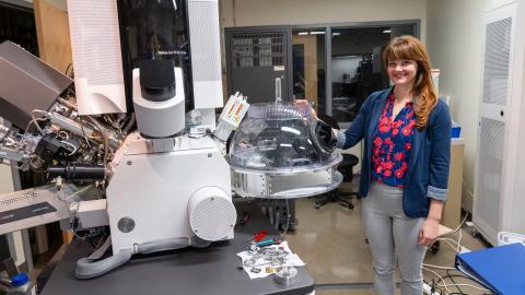Valerie Brogden poses next to the the Noble Dome, a transparent dome with gloves attached, connected directly to a microscope.