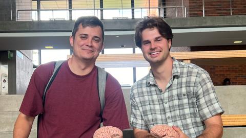 Two students sit on stairs in the Lewis Integrative Science Building, holding models of brains. 