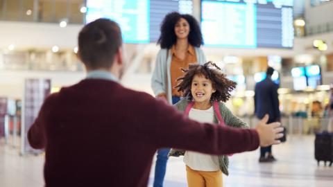 A happy young child running through an airport toward a person with their arms outstretched for a hug.