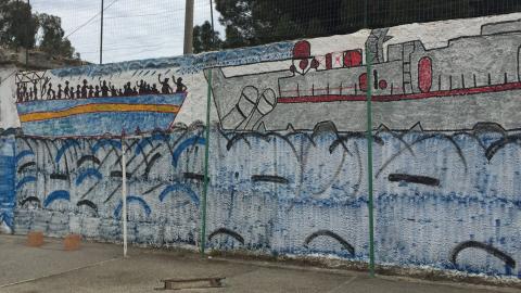 A mural of migrants on a boat painted on a wall.
