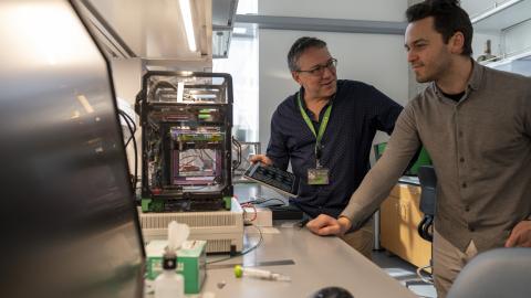 Two men talk to each other while standing in a lab.