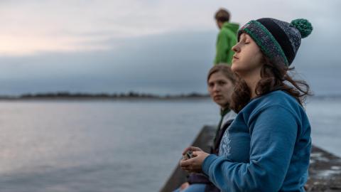 A student standing on a dock closes her eyes and turns her head toward the setting sun.