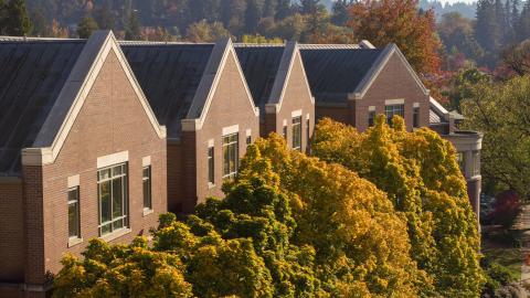 A red brick building lined on the front with trees with green, yellow, and orange leaves.
