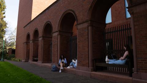 Three students sit and study outside the Jordan Schnitzer Museum of Art on a sunny day.