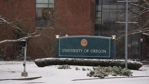 A light layer of snow blankets a sign reading University of Oregon.