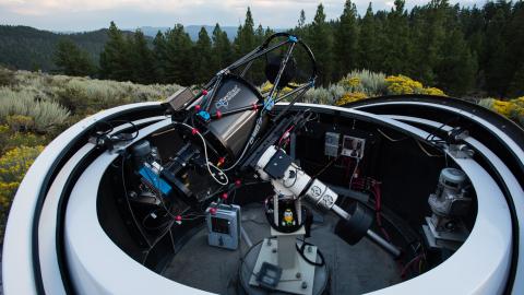A telescope at the Pine Mountain Observatory pointed toward the sky with hills and trees in the background.