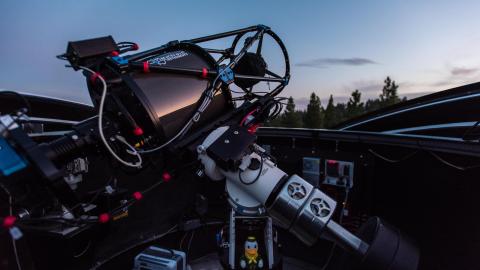 Large, high-tech telescope mounted inside an open observatory dome at dusk