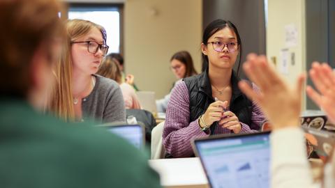 Four people sitting at a table have a discussion with computers open before them.