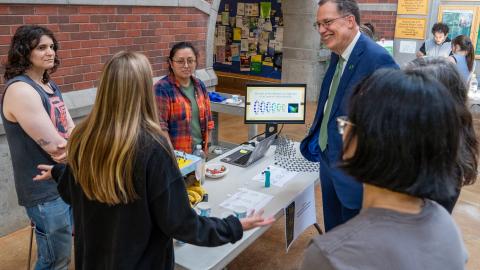 Students stand around a table in conversation with UO president John Karl Scholz.