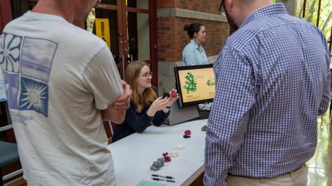 A person sitting at a table holds 3d printed objects in her hands while talking to people standing around the table.