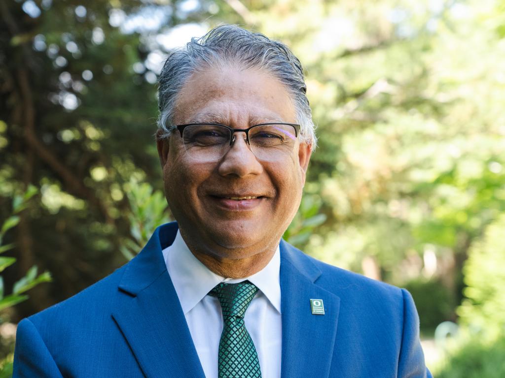 Man in suit and tie with glasses smiled in front of trees