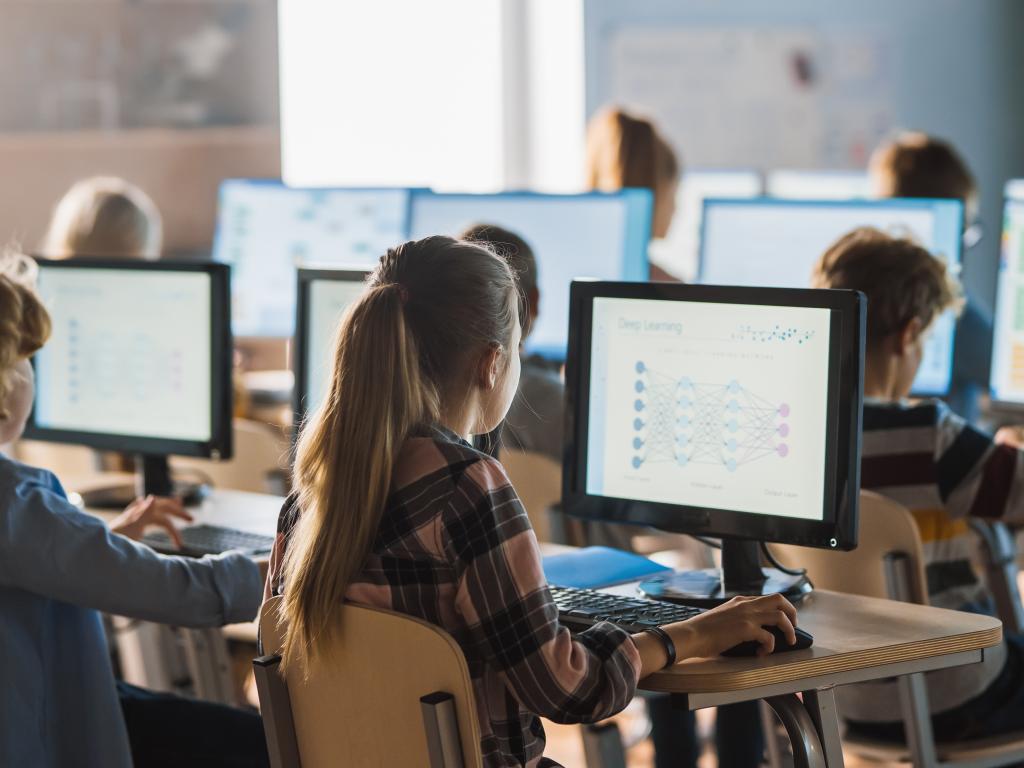Class of children sit in computer lab working on monitors