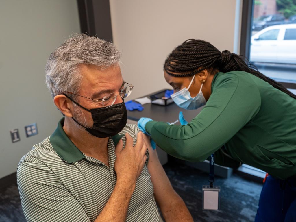 A person wearing a face mask receives a vaccination from another person wearing a face mask.