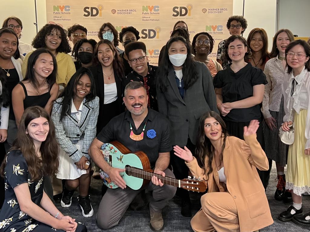 A large group of students surrounding Ernesto Martínez who is holding a painted guitar. 