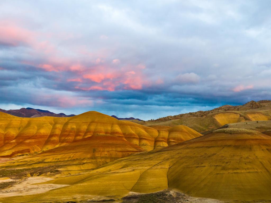 Colorful pink and purple clouds fill the sky over the painted hills of John Day. The hills are striped with orange, yellow, and red.