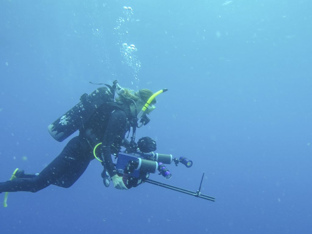 A woman underwater wearing scuba gear and holding a camera.