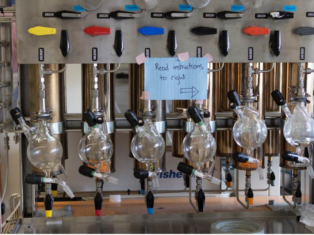 A machine with different colored levers and glass bottles. A sign is taped on it that says ‘read instructions to right’ with an arrow.