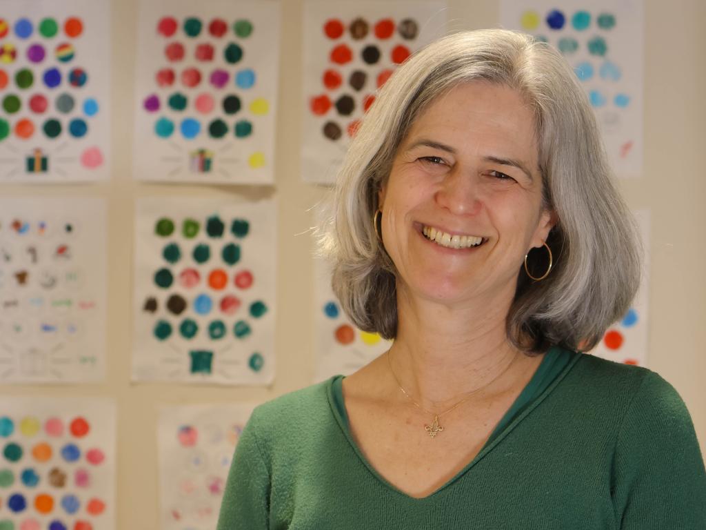 Melissa Redford posing next to a wall of colorful worksheets that children use to keep track of their progress in the study.