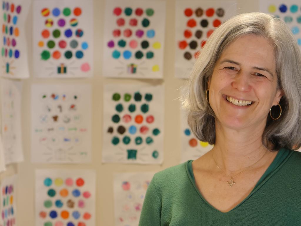 Melissa Redford posing next to a wall of colorful worksheets that children use to keep track of their progress in the study.