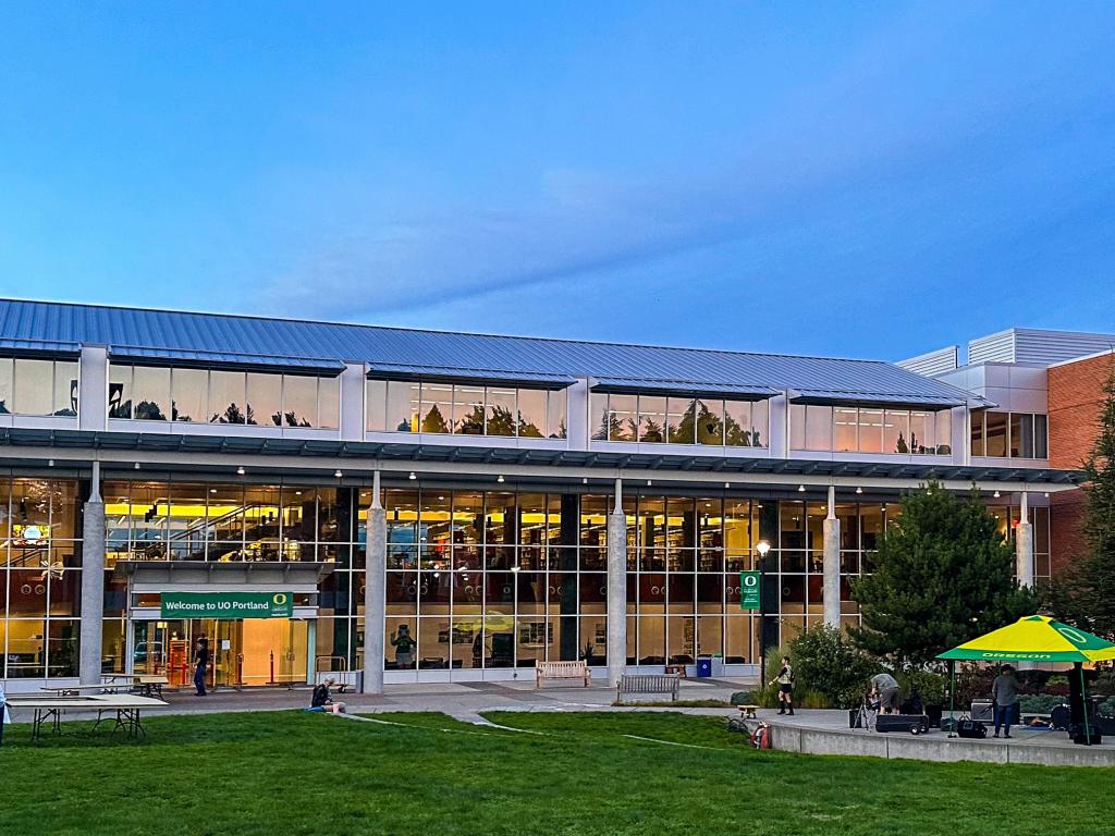 The UO Portland library building at dusk with lights on inside the building.