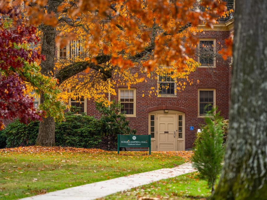 Trees full of bright red and orange fall leaves frame a red brick building.