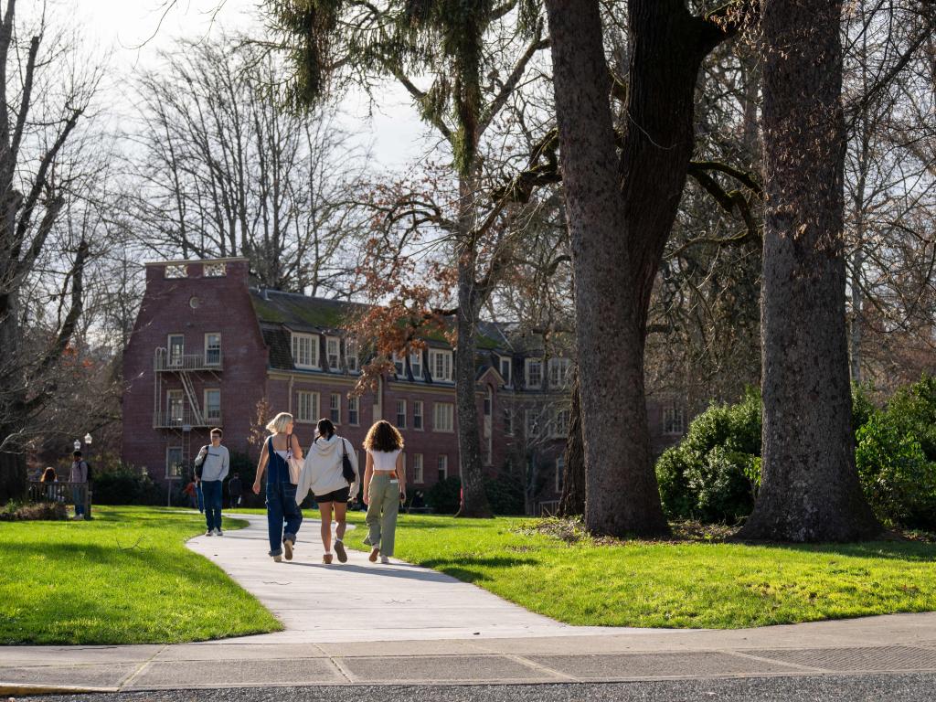 Students walking on a campus path between buildings on a sunny winter day.
