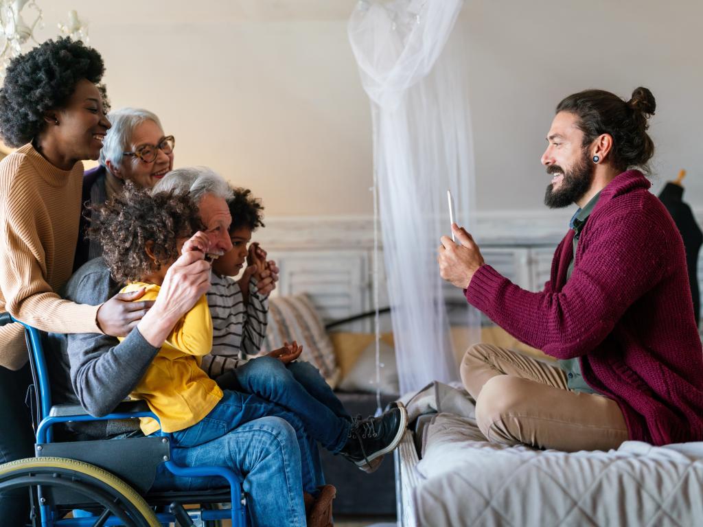 A person sitting on a bed takes a photo of a group of smiling kids and adults.